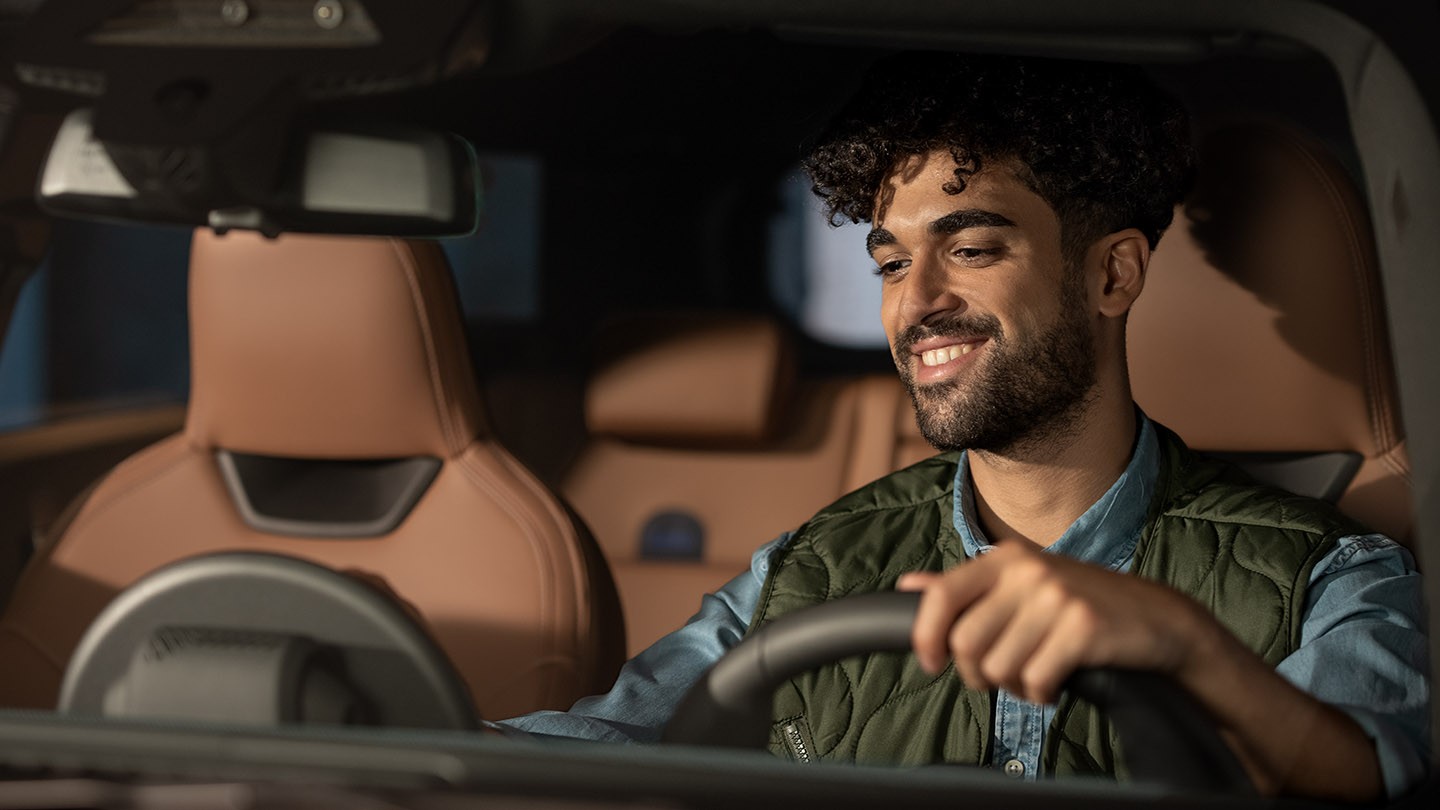 Ein junger Mann sitzt lächelnd in einem MINI Countryman und bedient währendessen das Display Ein junger Mann sitzt lächelnd in einem MINI Countryman und bedient währendessen das Display